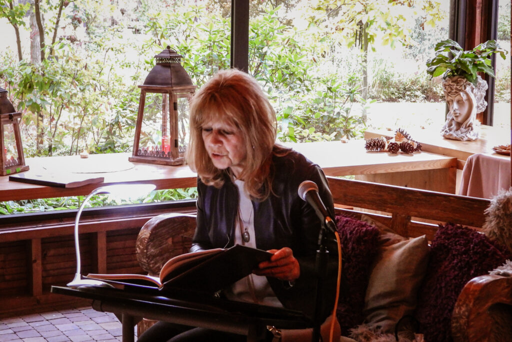 na pierwszym planie widać kobietę, która czyta książkę, jest lekko pochylona do przodu, z tyłu widać duży lampion a za nim okno z widokiem na ogród Daglezja na zielonej w Rykach