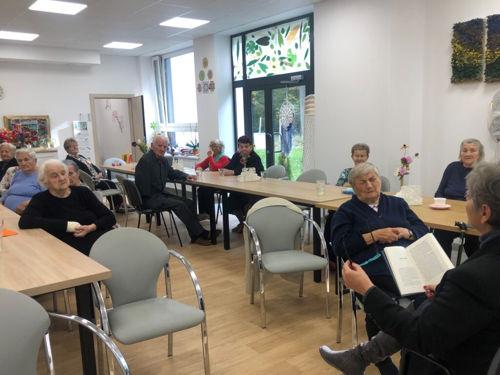 Dzienny Dom Opieki medycznej w Stawach, na sali seniorzy słuchają czytanej książki