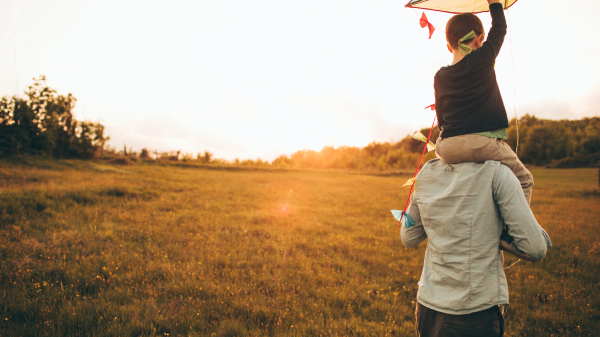 zachód słońca, ojciec niesie na barana dziecko, ujęcie tyłem