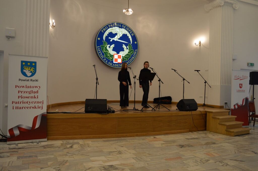 Przegląd Piosenki Patriotycznej i Harcersskij Powiatowej Biblioteki Publicznej w Rykach, scena, dwie osoby śpiewają w mundurkach