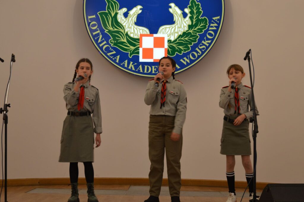 Przegląd Piosenki Patriotycznej i Harcersskij Powiatowej Biblioteki Publicznej w Rykach, troje harcerzy na scenie scena