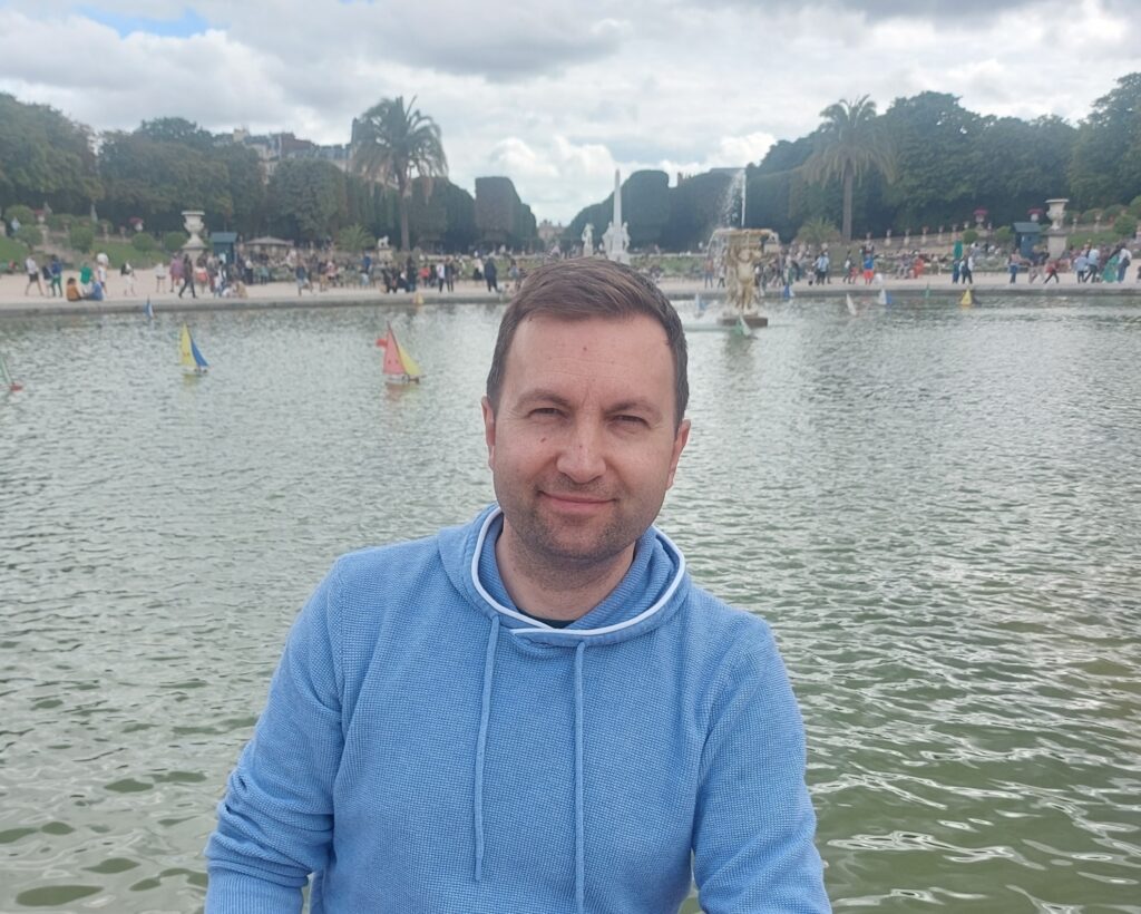 dr Marcin Lutomierski w niebieskiej bluzie na tle jeziora