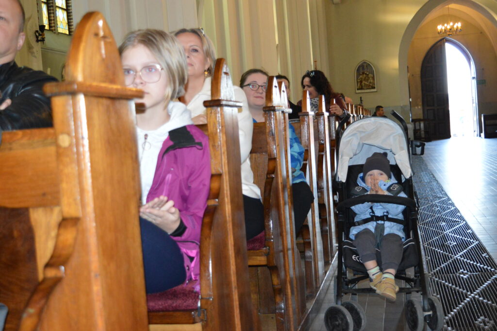 w Kościele dziecko w w wózku patrzy na uczestników konkursu na najciekawsze wykonanie montażu słowno-muzycznego poświęconego pamięci świętemu Jana Pawła drugiego
