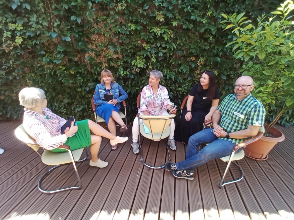 5 osób siedzi na dworze na szkoleniu, rozmawiają, to szkolenie coachingowe dla dyrektorów bibliotek