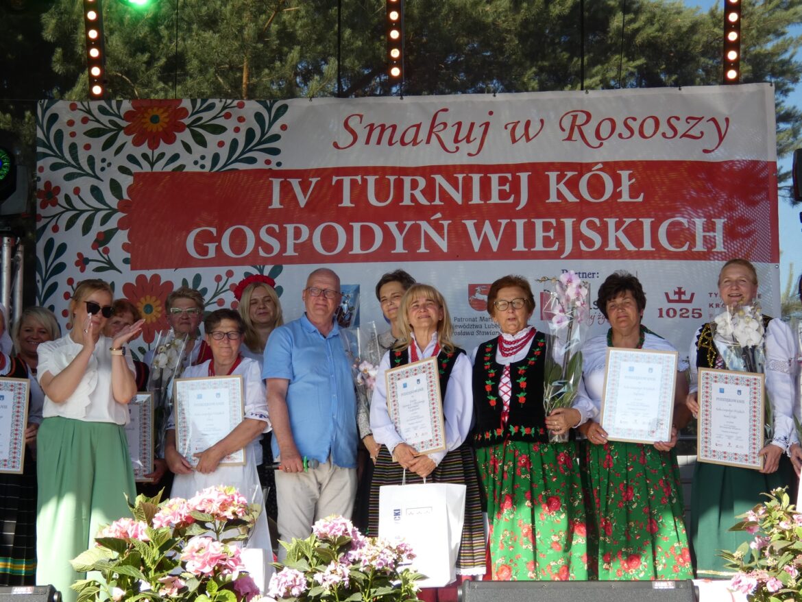 g 4 turniej KGW w Rososzy, zwycięzcy stoją na tle dużego plakatu w strojach ludowych, starosta pozuje do zdjęcia