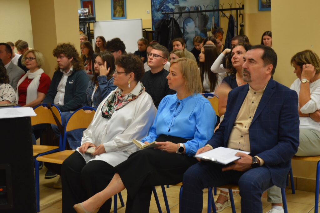 widownia siedzi, słucha, z boku żółte słoneczniki, tło narodowe czytanie, scena