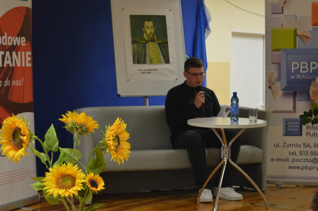 Czyta młodzieniec, siedzi, z boku żółte słoneczniki, tło narodowe czytanie, scena