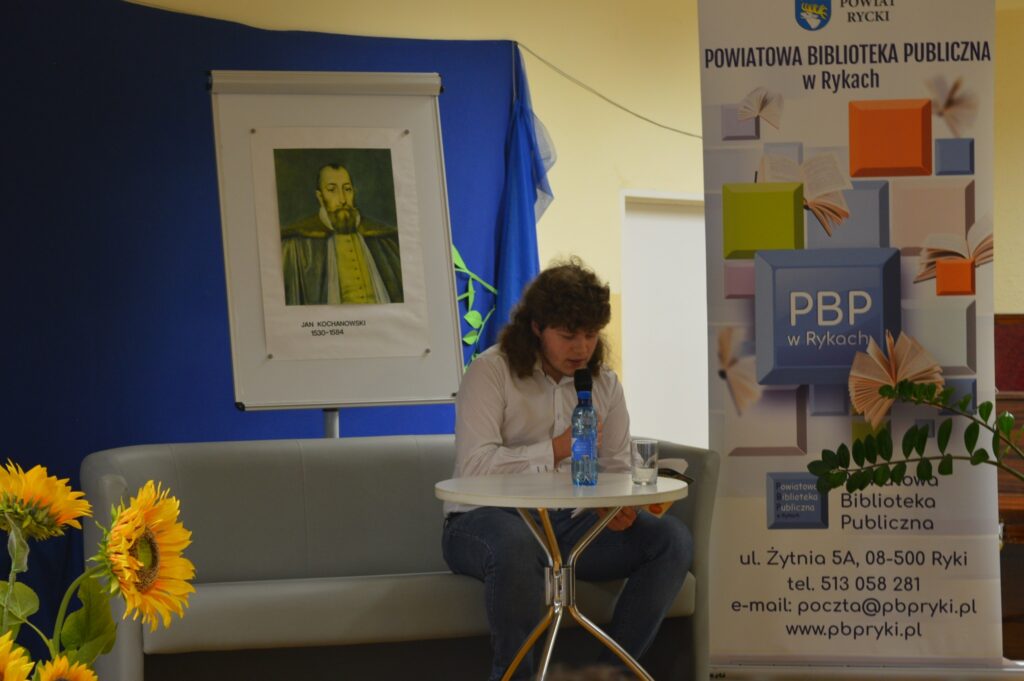 Czyta młodzieniec, siedzi, z boku żółte słoneczniki, tło narodowe czytanie, scena