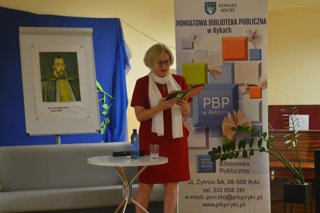 Czyta nauczycielka, stoi, czerwona sukia, z boku żółte słoneczniki, tło narodowe czytanie, scena