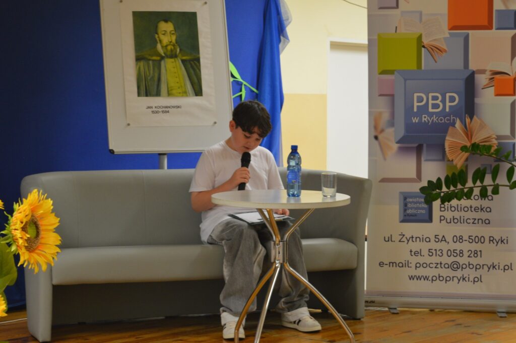 Czyta młodzieniec, siedzi, z boku żółte słoneczniki, tło narodowe czytanie, scena