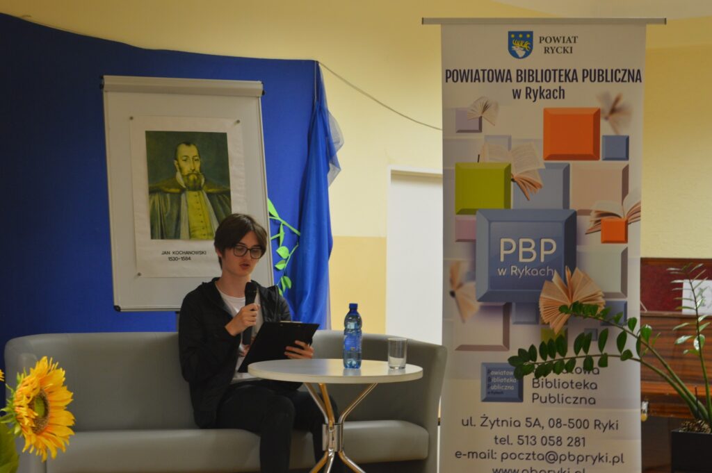 Czyta młodzieniec, siedzi, z boku żółte słoneczniki, tło narodowe czytanie, scena