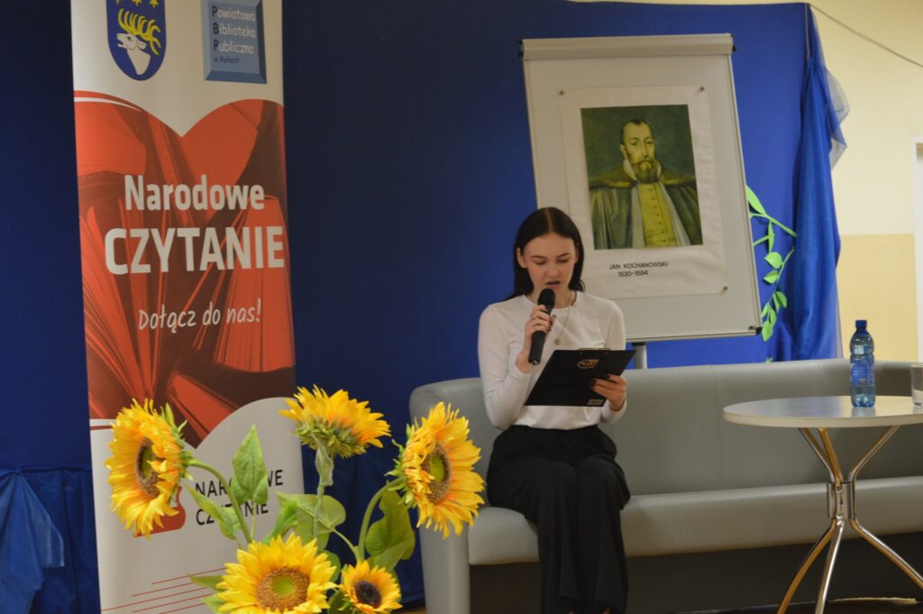 Czyta dziewczyna, siedzi, z boku żółte słoneczniki, tło narodowe czytanie, scena