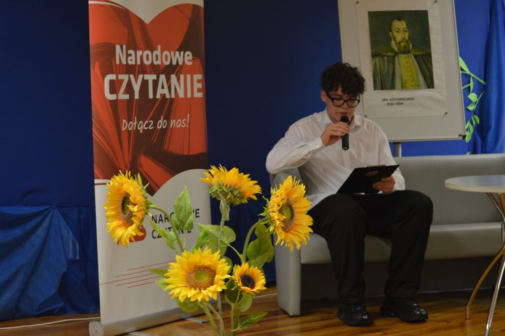 Czyta młodzieniec, siedzi, z boku żółte słoneczniki, tło narodowe czytanie, scena