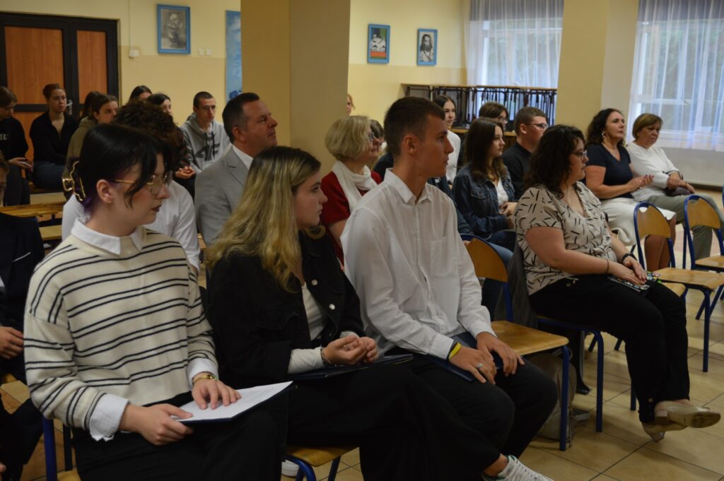 widownia siedzi, słucha, z boku żółte słoneczniki, tło narodowe czytanie, scena